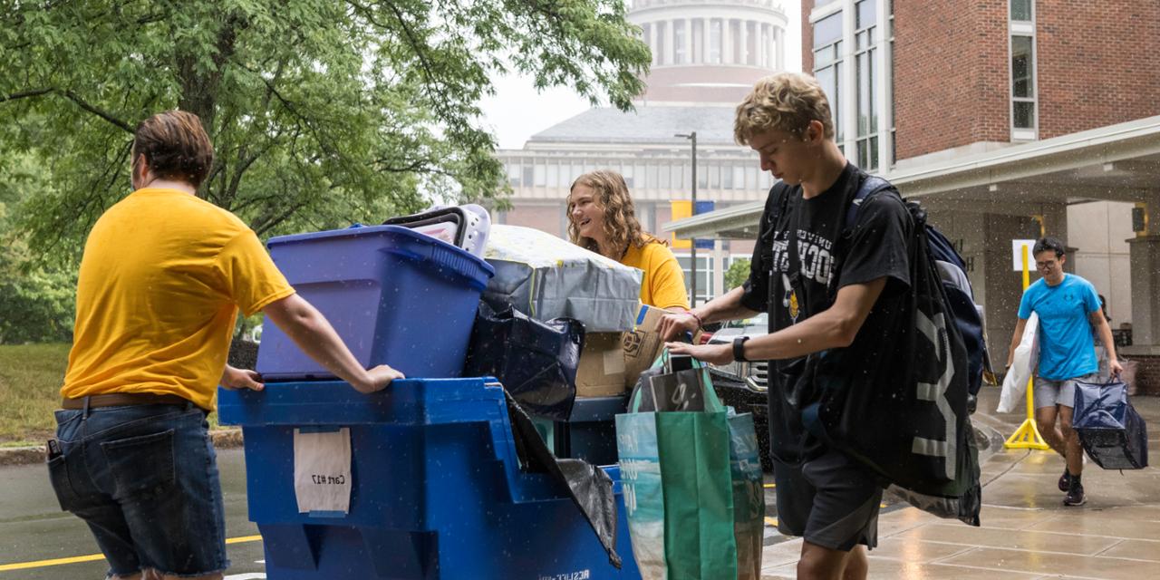 Students transport belongings in a large rolling bin on move-in day